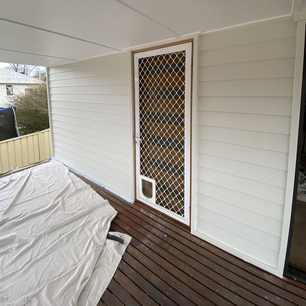Freshly installed white weatherboard cladding beside a screen door on a timber deck